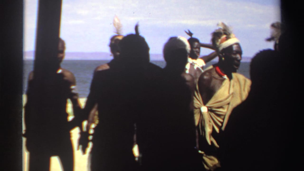 Men in silhouette and traditional dress stand near vertical posts with water behind them.