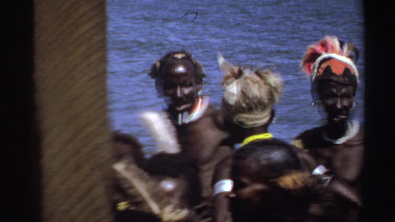 Group members in headwear and armbands stand by water with a vertical obstruction in front.