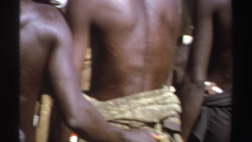 1969 Sudan home-movie frame showing a close rear view of a shirtless person within a tightly gathered outdoor crowd.