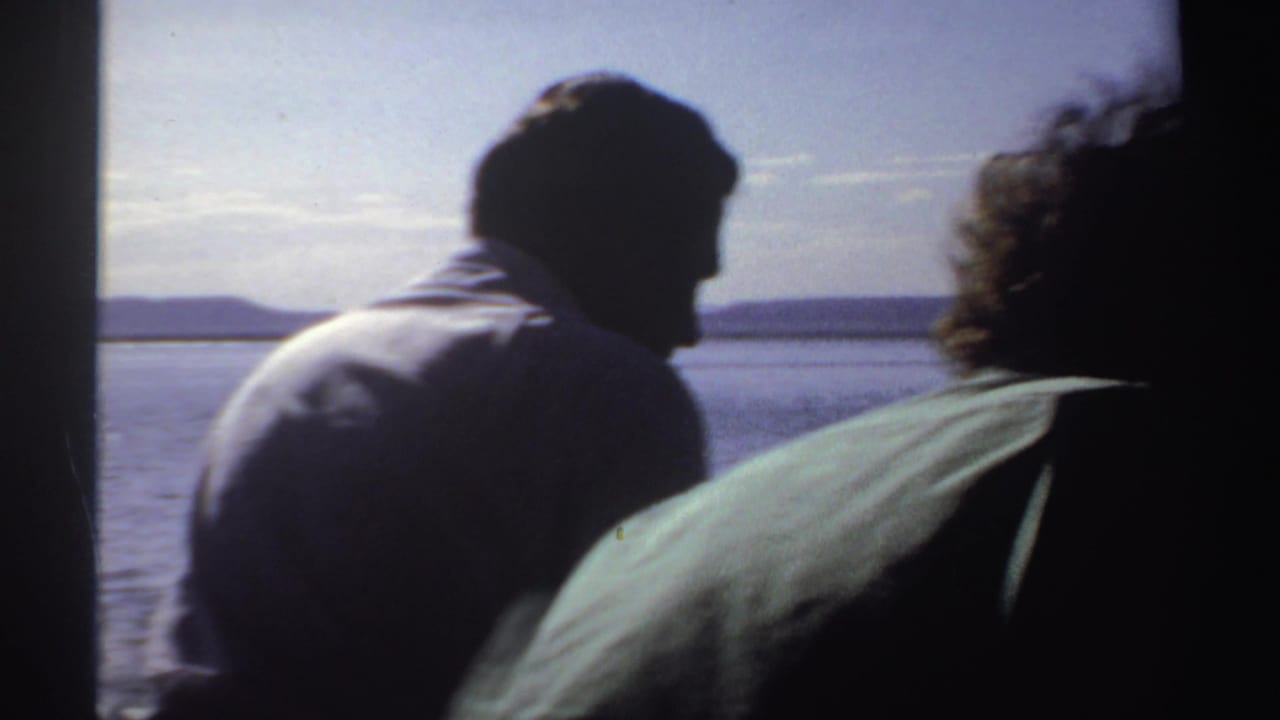 1969 Sudan 8mm frame showing silhouetted adults on a small boat against bright rippled water and a low distant shoreline.