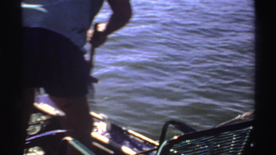 Backlit 1969 Sudan frame showing a standing figure on a small boat holding a pole or line over shimmering water.
