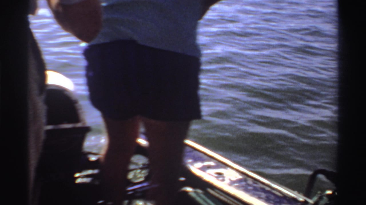 1969 Sudan 8mm frame showing an adult in shorts on a small boat near bright rippled water and a partly seen motor.