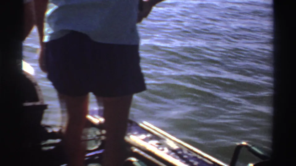 1969 Sudan home-movie frame showing an adult near the stern of a small boat with water behind.