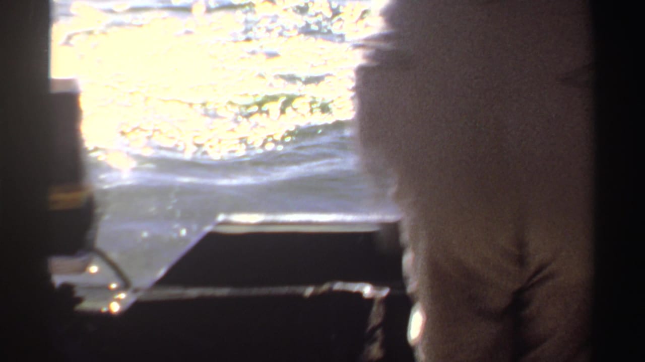Adult standing on a boat beside sunlit rippling water.