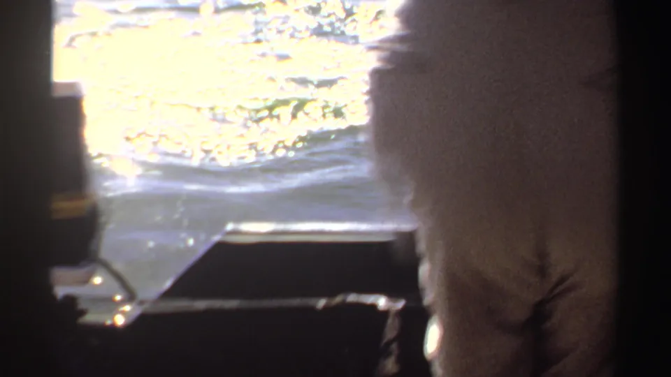 1969 Sudan 8mm frame showing an adult on a small boat, with bright reflections across lake water.