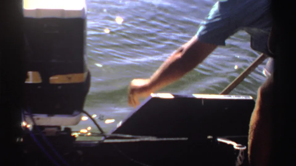 1969 Sudan home-movie frame of an adult leaning from a boat toward sunlit lake water.
