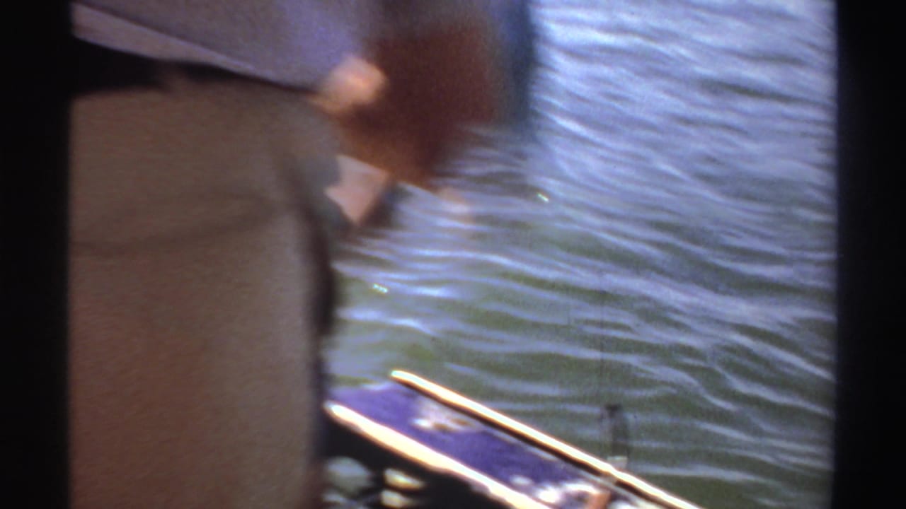 Men standing on a boat beside rippling water, partly obscured by dark frame edges.