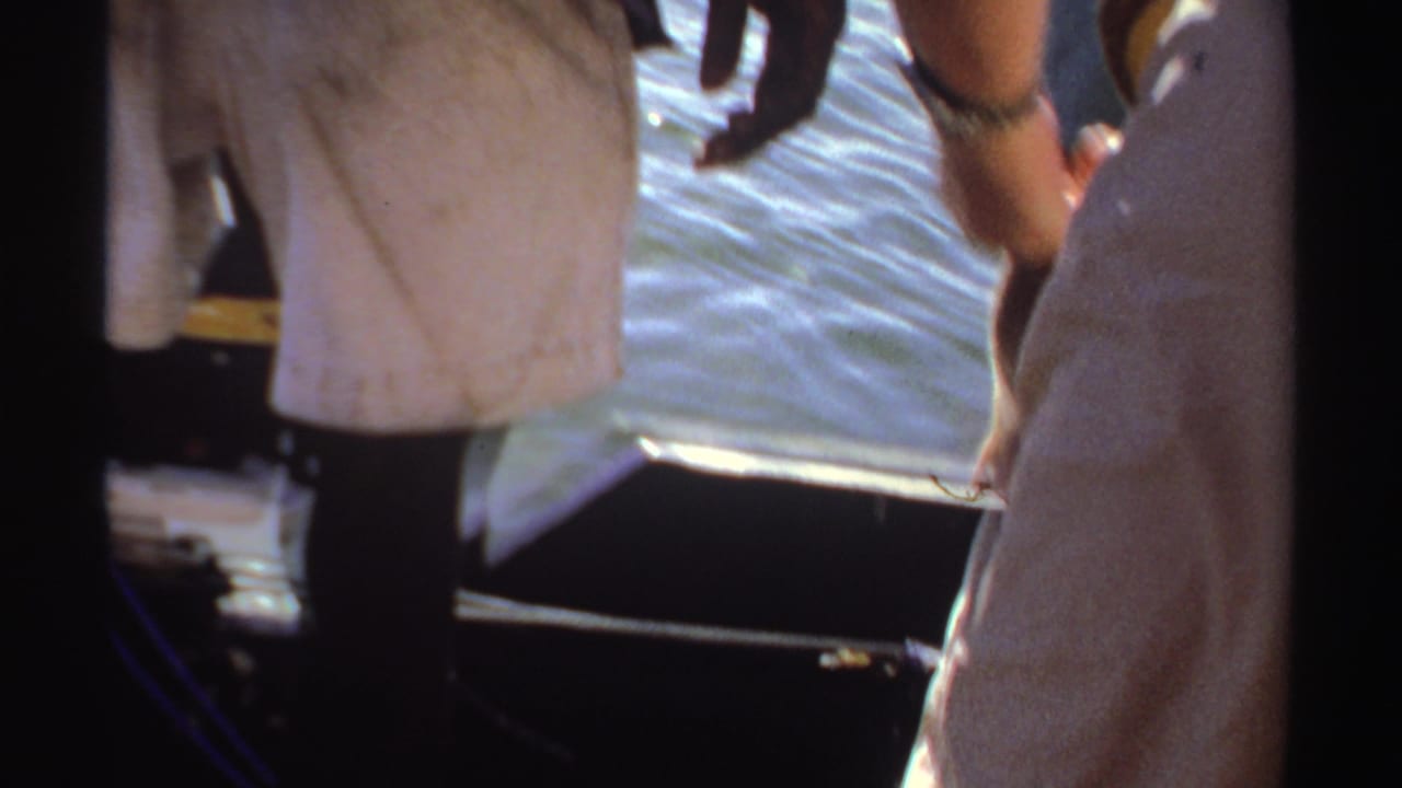 Close view of legs, hands, a towel, boat edge, and rippled water.
