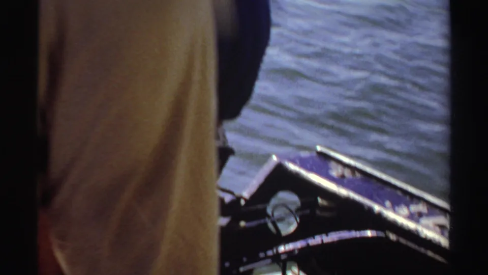 1969 Sudan 8mm frame looking down toward a boat edge, rippled water, clothing, and a dark object or gear near the bottom of the frame.
