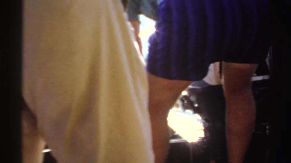 1969 Sudan 8mm frame showing lower bodies on a small boat, a dark blue garment, pale fabric, water, and strong reflected sunlight.