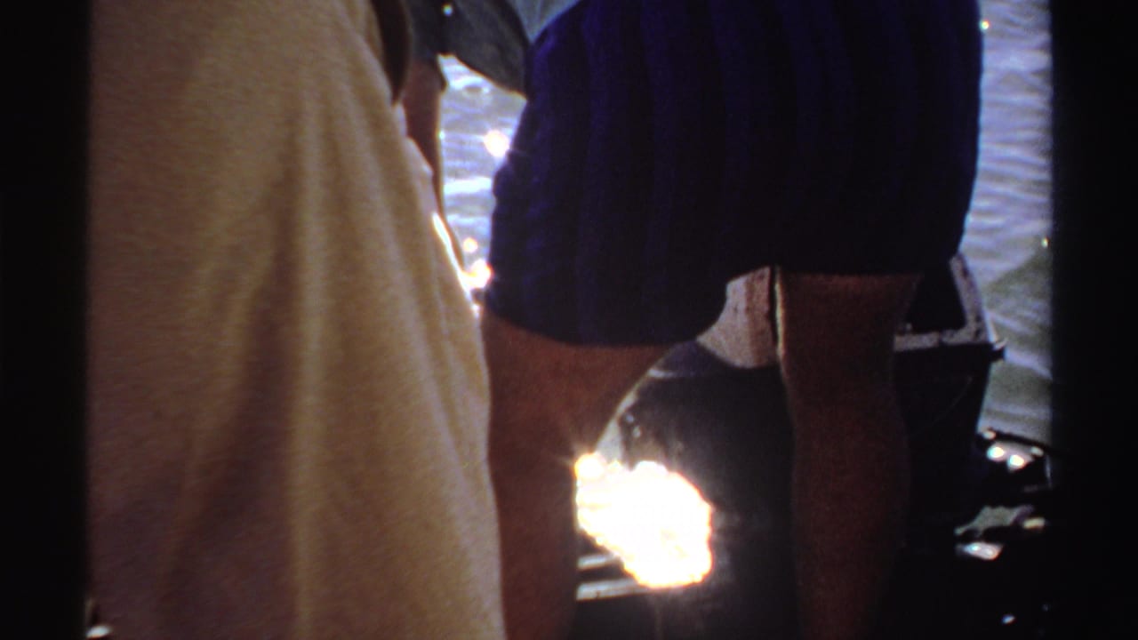 In this 1969 Sudan 8mm frame, people stand near shimmering water as a fishing line drops toward the surface.