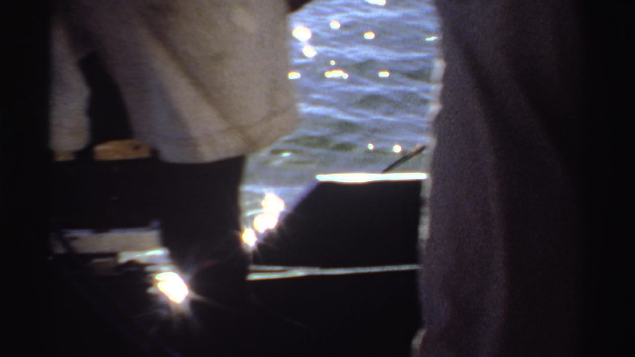 A close 8mm view shows people standing by the water in Sudan, with sunlight reflecting strongly behind them.