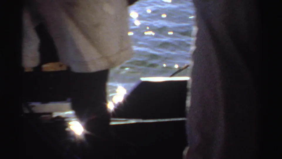 A close 8mm view shows people standing by the water in Sudan, with sunlight reflecting strongly behind them.