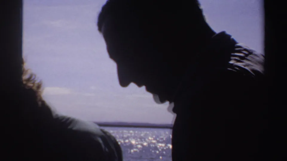 1969 Sudan 8mm frame showing silhouetted adults on a boat, with one profile leaning toward sunlit water.