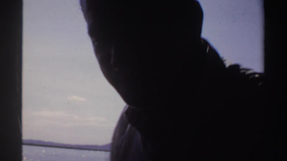 1969 Sudan 8mm frame showing a shaded adult figure near a boat rail, with open water and sky in the background.
