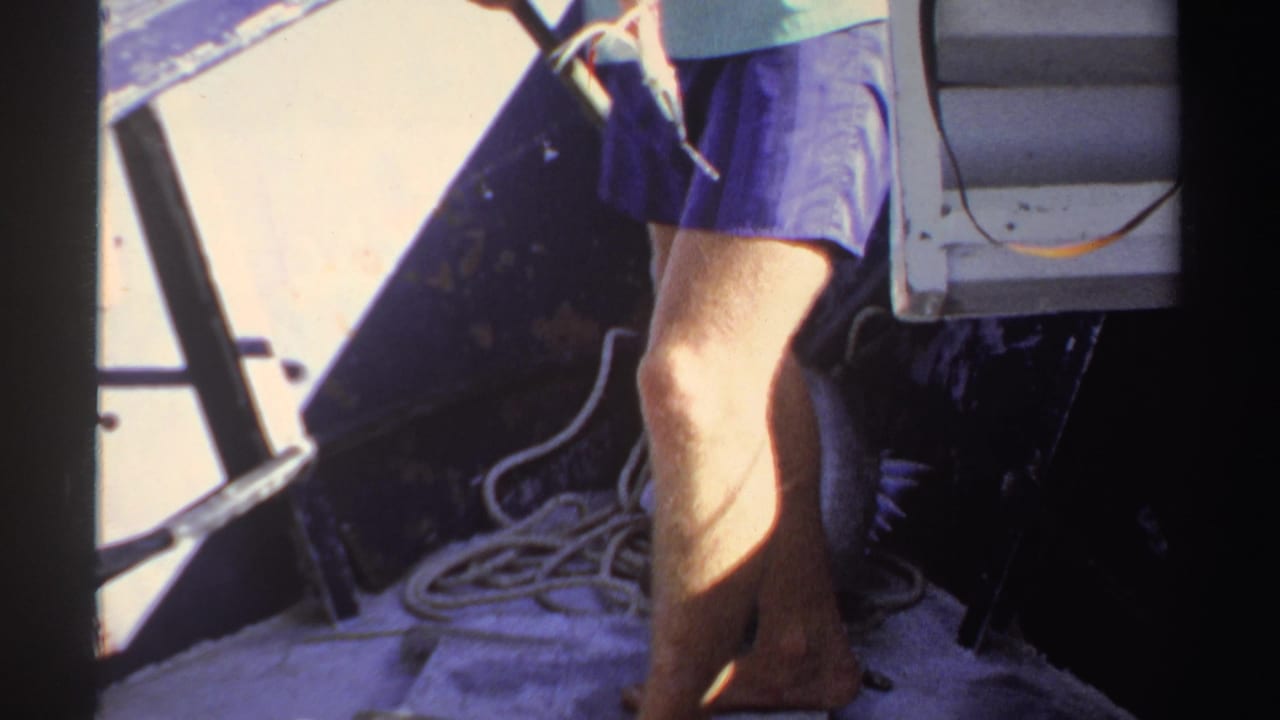 Adult's legs pass near rope and a fish on a small boat deck.