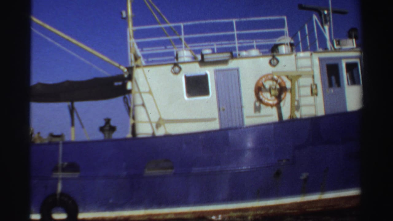 Blue fishing boat with a white cabin, railings, ropes, and life preserver.