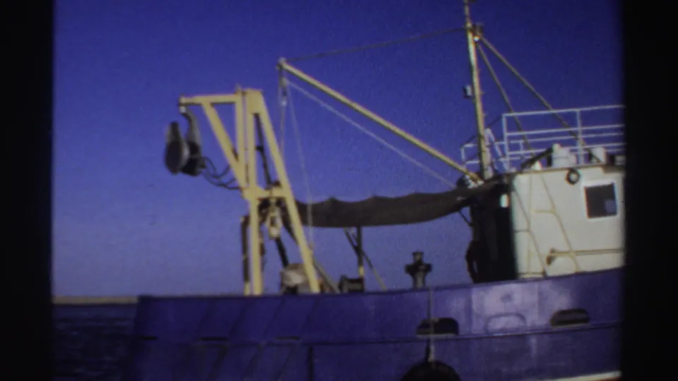 1969 Sudan 8mm frame with the bow-side deck area of a blue boat, yellow crane, rigging, and white cabin visible.