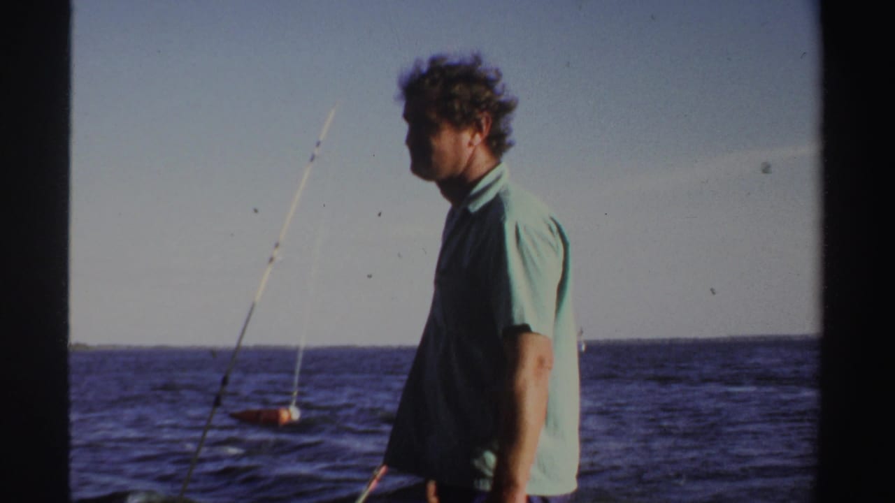 1969 Sudan 8mm frame with an adult man in a light green shirt standing on deck near fishing rods and open water.