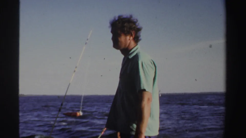 1969 Sudan 8mm frame with an adult man in a light green shirt standing on deck near fishing rods and open water.