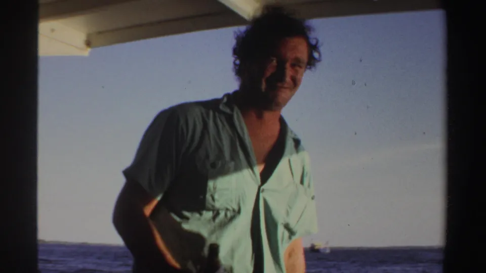 In 1969 Sudan-associated 8mm footage, a smiling man faces the camera on a boat with open water and sky behind him.
