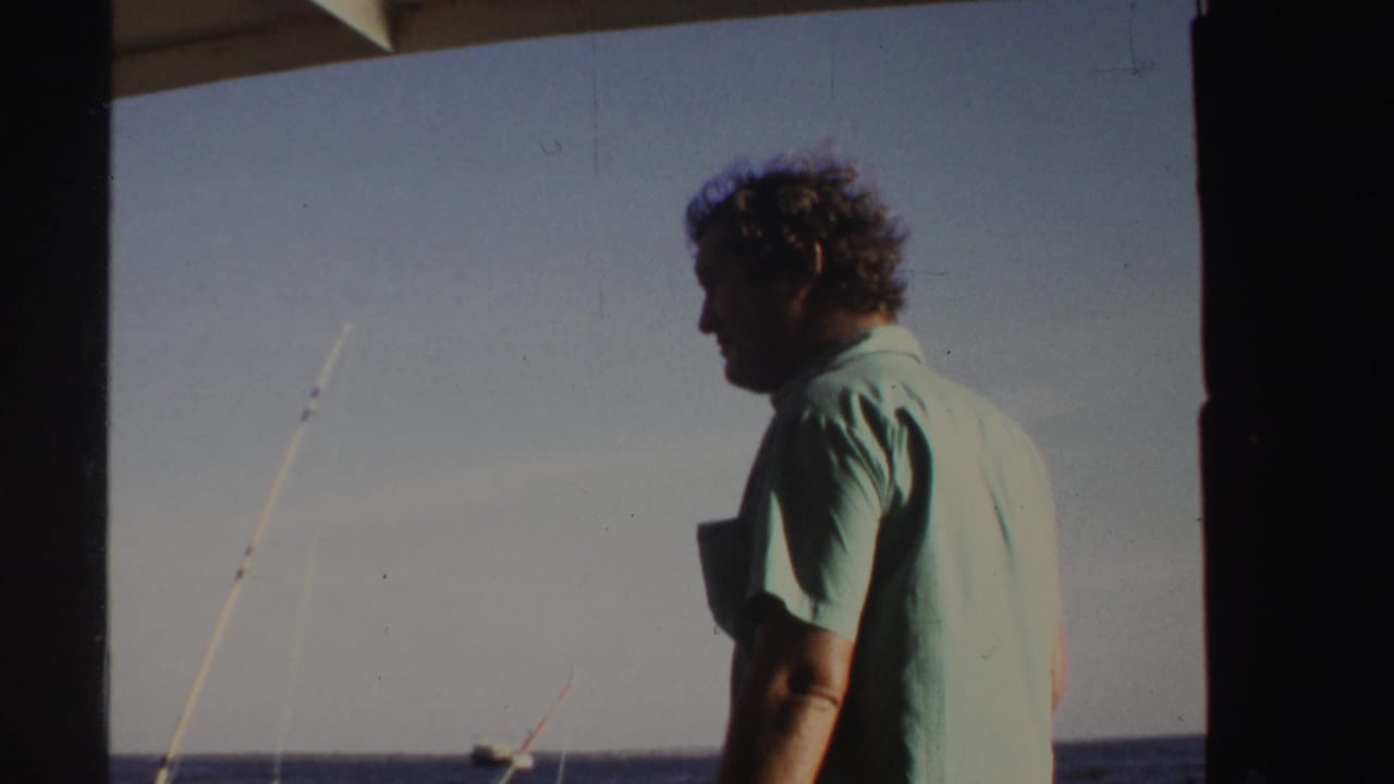 Man in profile on a boat with fishing rods and water behind him.