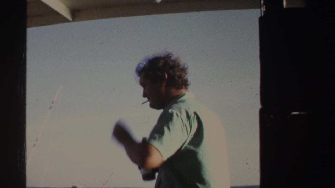 Man in a light blue shirt smokes while standing on a boat.