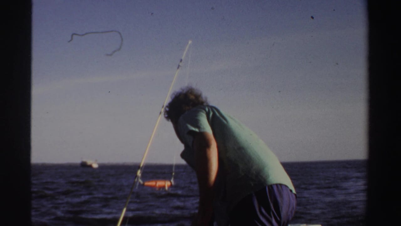 The man bends over the boat deck while a fishing rod angles upward and open water fills the background in Sudan, 1969.