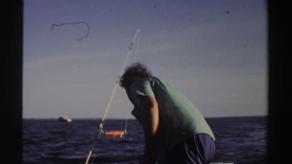 The man bends over the boat deck while a fishing rod angles upward and open water fills the background in Sudan, 1969.