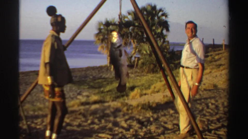 Near the end of the 1969 Sudan clip, a second man in light clothing stands beside the beach tripod scale and suspended fish.