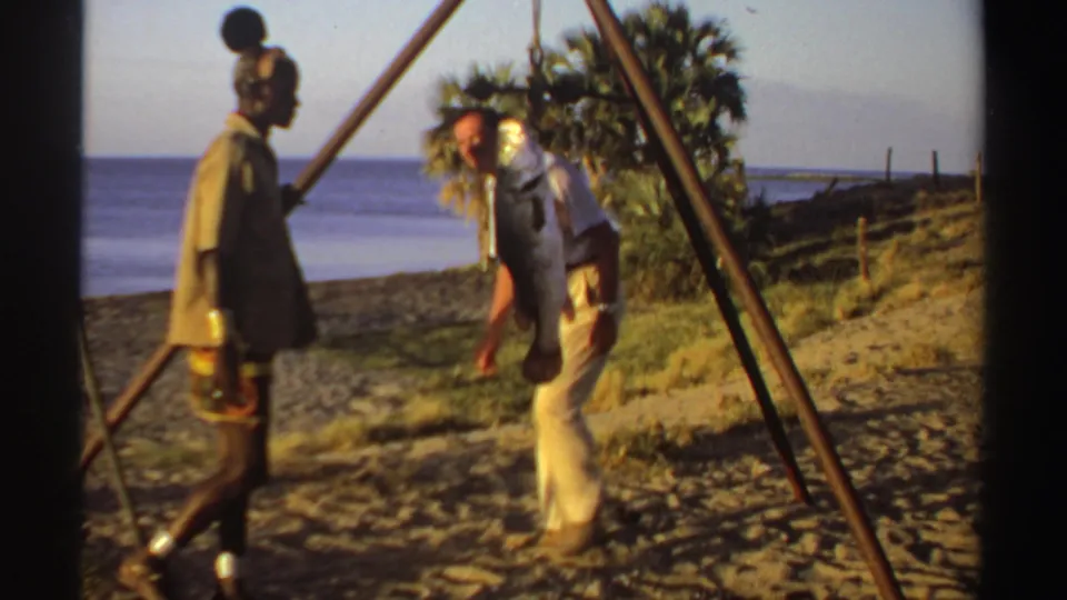 The visitor bends down beside the suspended catch as the fisherman remains in profile on the Sudan beach.