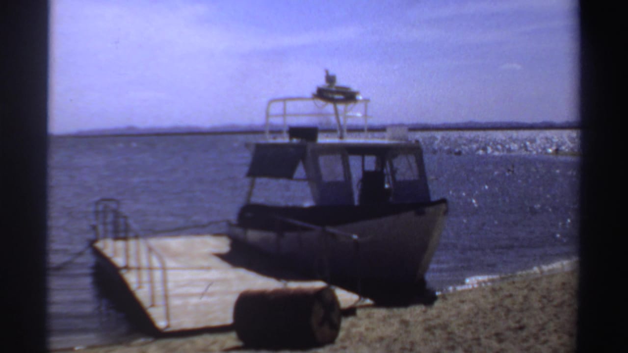 Cabin motorboat moored next to a wooden pier with rippling water and low distant shoreline.