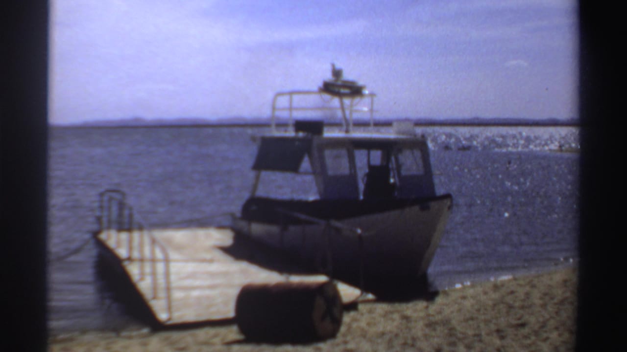 Small powerboat tied beside a wooden dock on a sandy shore.