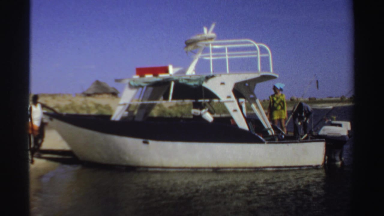 White motorboat on a sandy shore with several people standing near the stern and cabin.