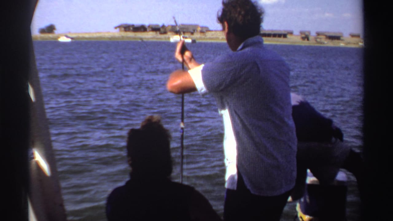 Man in a light shirt fishes from a boat while passengers sit near rippling water.