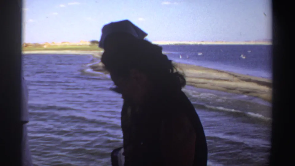 1969 Sudan 8mm frame of a silhouetted adult on a boat, looking toward water and a low shoreline under bright sky.