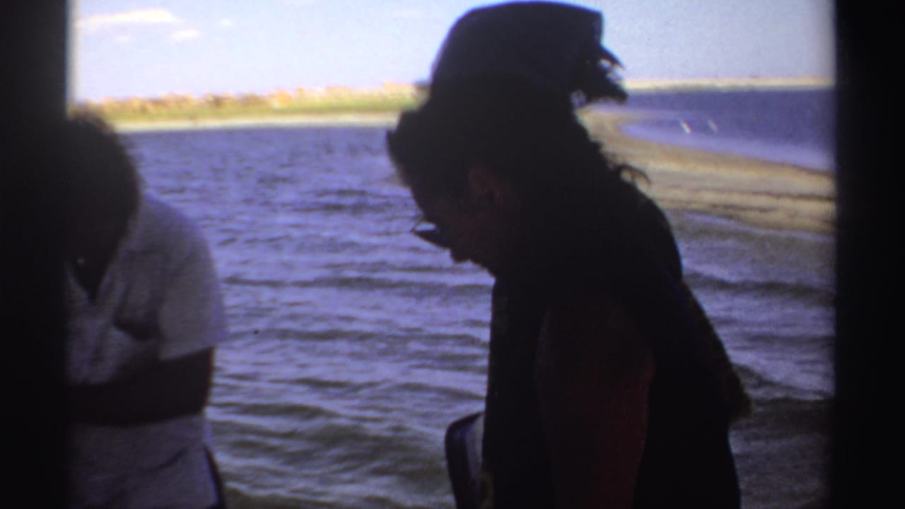 Adults aboard a boat, with one person in a dark hat leaning near the water.