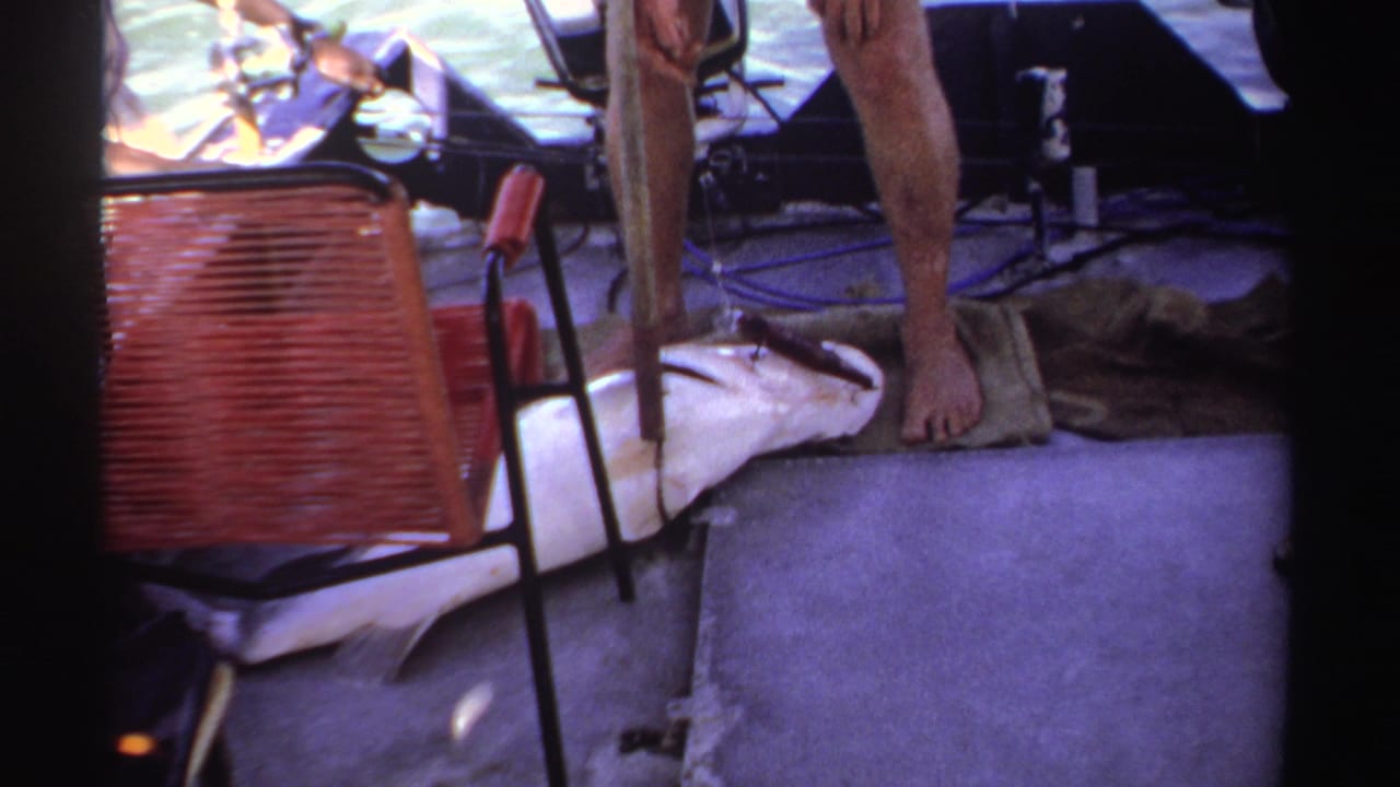 Large fish on a small boat deck beside bare feet and fishing gear.