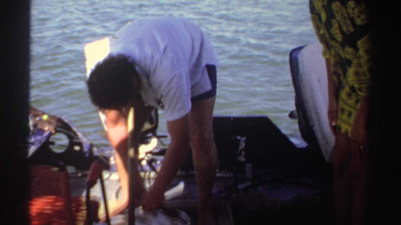A man leans down near fishing gear on a small boat in Sudan, with a woman in a white headscarf standing beside him.