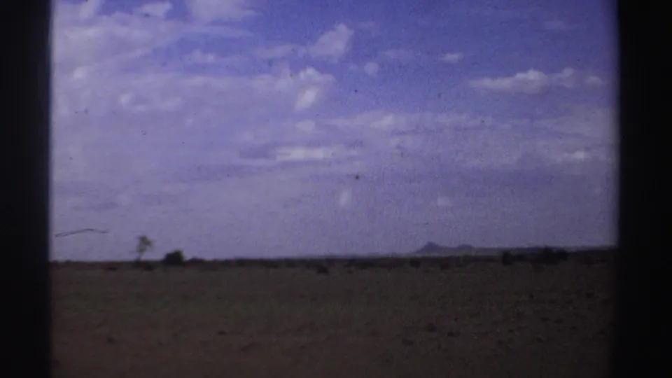 A wide Sudan landscape appears in the 1969 8mm footage, with open ground, low horizon, and clouded sky.