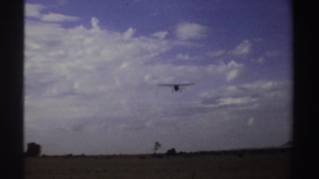 The aircraft remains small in the frame as it flies over a low Sudanese horizon, with cloud banks and open ground below.