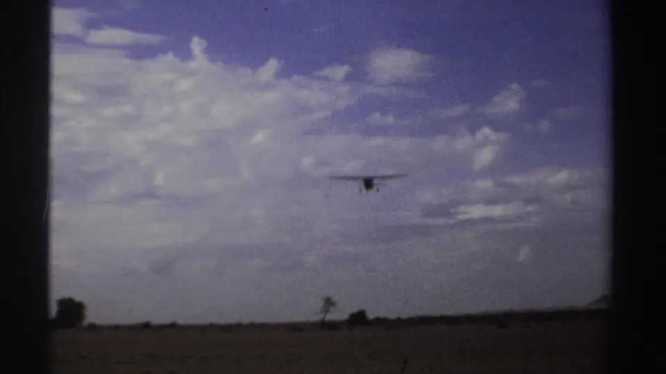 The aircraft remains small in the frame as it flies over a low Sudanese horizon, with cloud banks and open ground below.