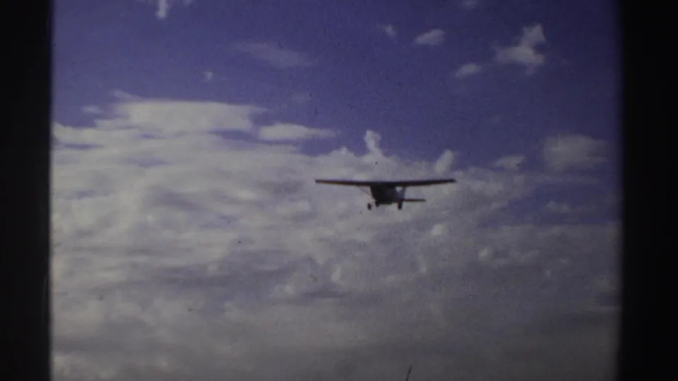 In 1969 Sudan 8mm footage, the aircraft appears closer against a textured blue and grey sky with little ground visible.