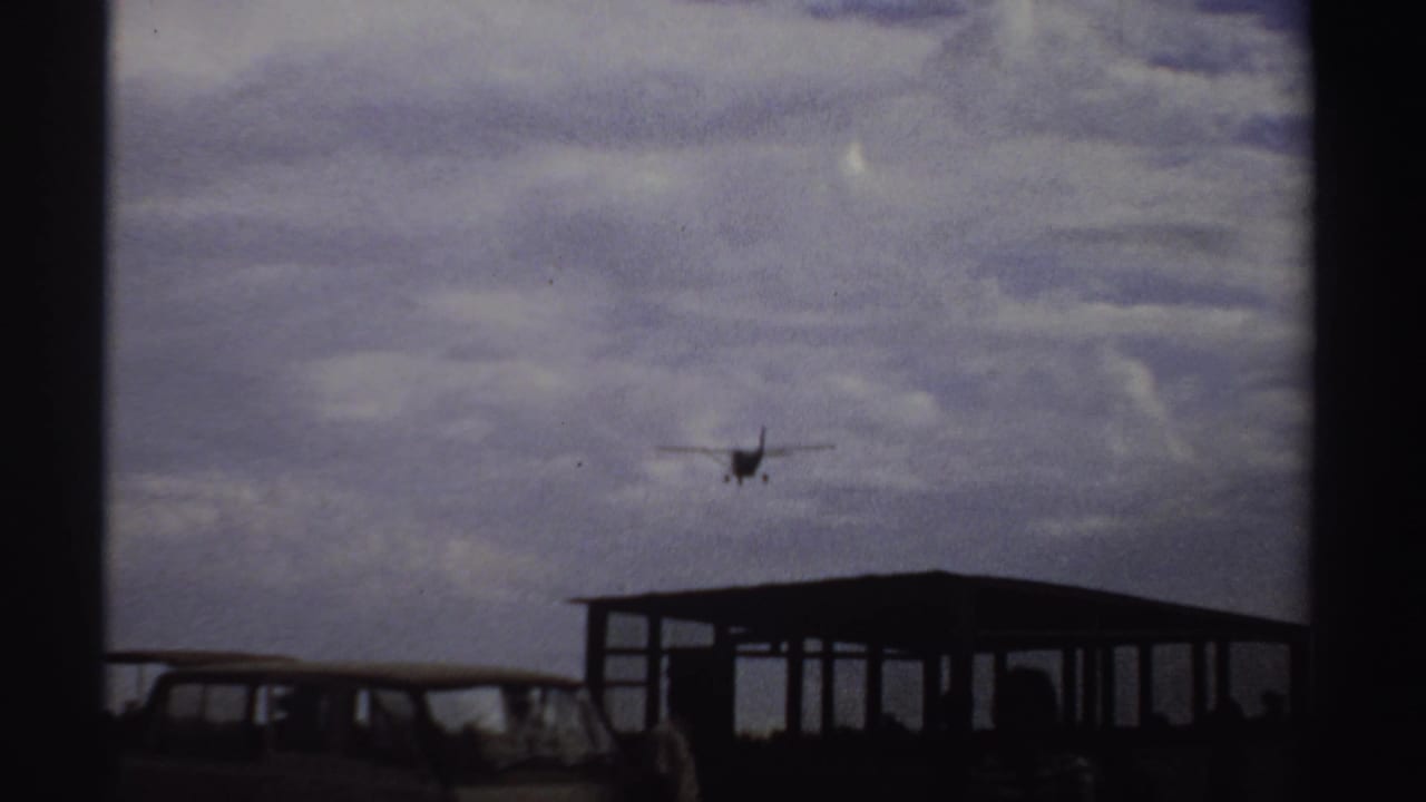 Plane descends over a parked van and open shelter.