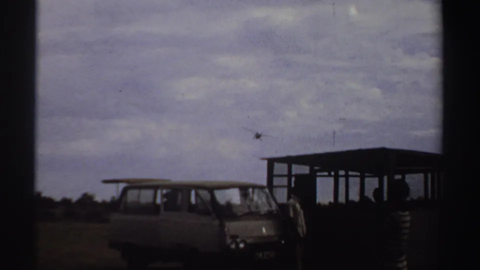 In 1969 Sudan home-movie footage, a small airplane approaches over a white van and people near an open airstrip shelter.