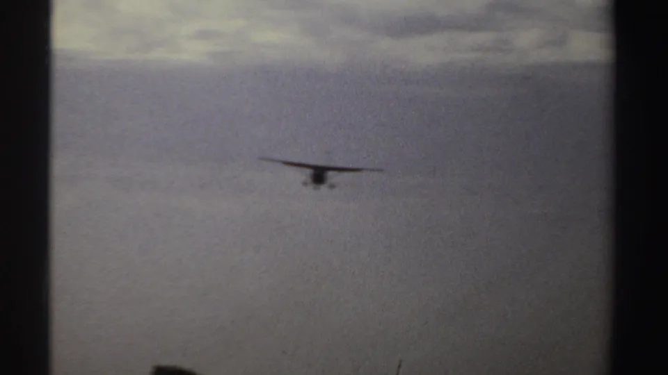 A small propeller plane draws closer over a broad, flat Sudan landscape in grainy 8mm footage.