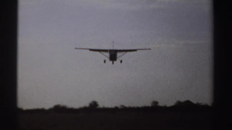 1969 Sudan 8mm frame showing a small propeller aircraft nearing landing over a rural treeline.