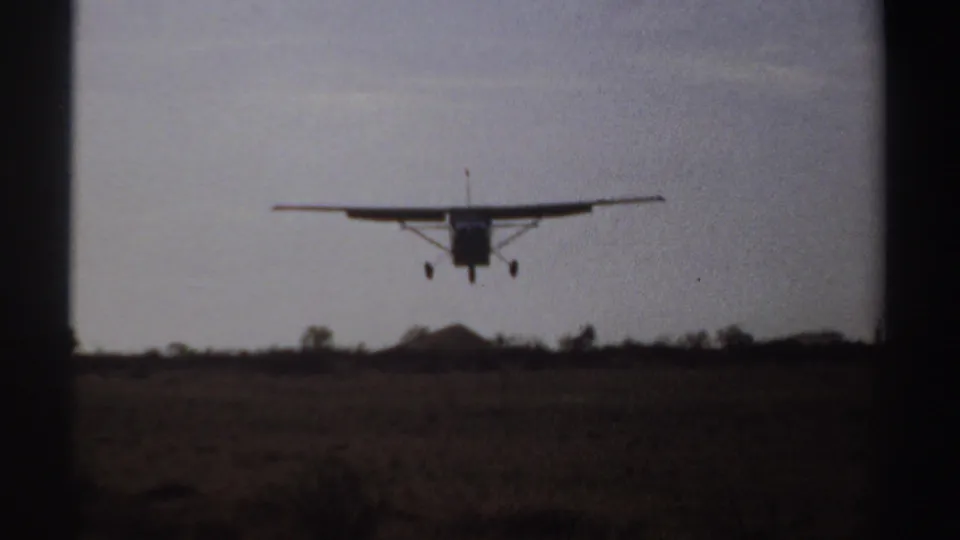 1969 Sudan 8mm frame showing a small aircraft moments before landing over open rural ground.