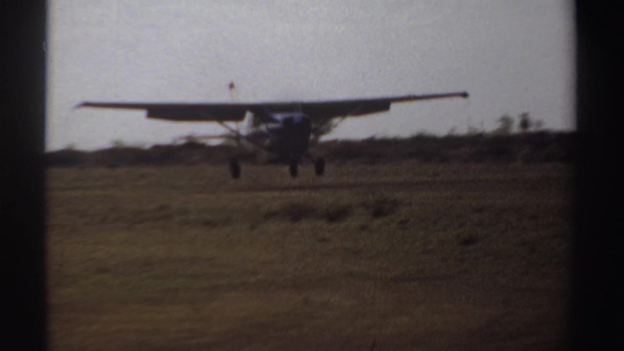 Small propeller aircraft descending toward a grassy landing field.