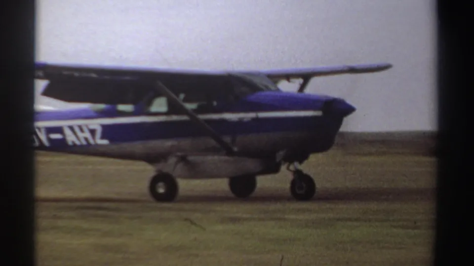 Side view of a blue and white high-wing aircraft taxiing on a Sudan field, with partial registration lettering visible.